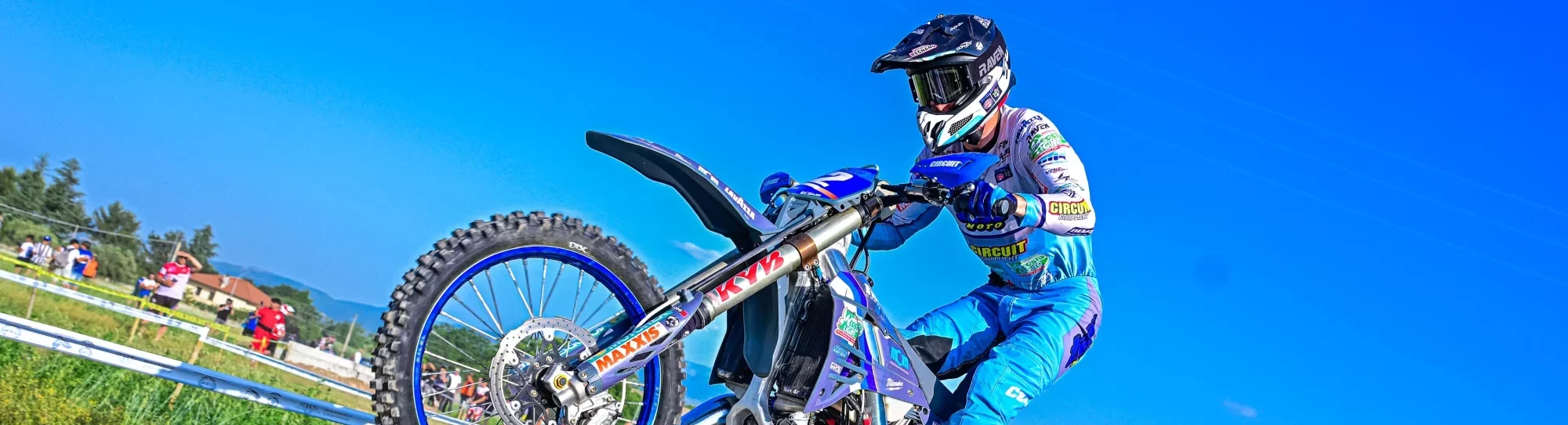 Motorcrosser in blauwe outfit rijdt over een rotsachtig parcours tijdens een wedstrijd op een zonnige dag.