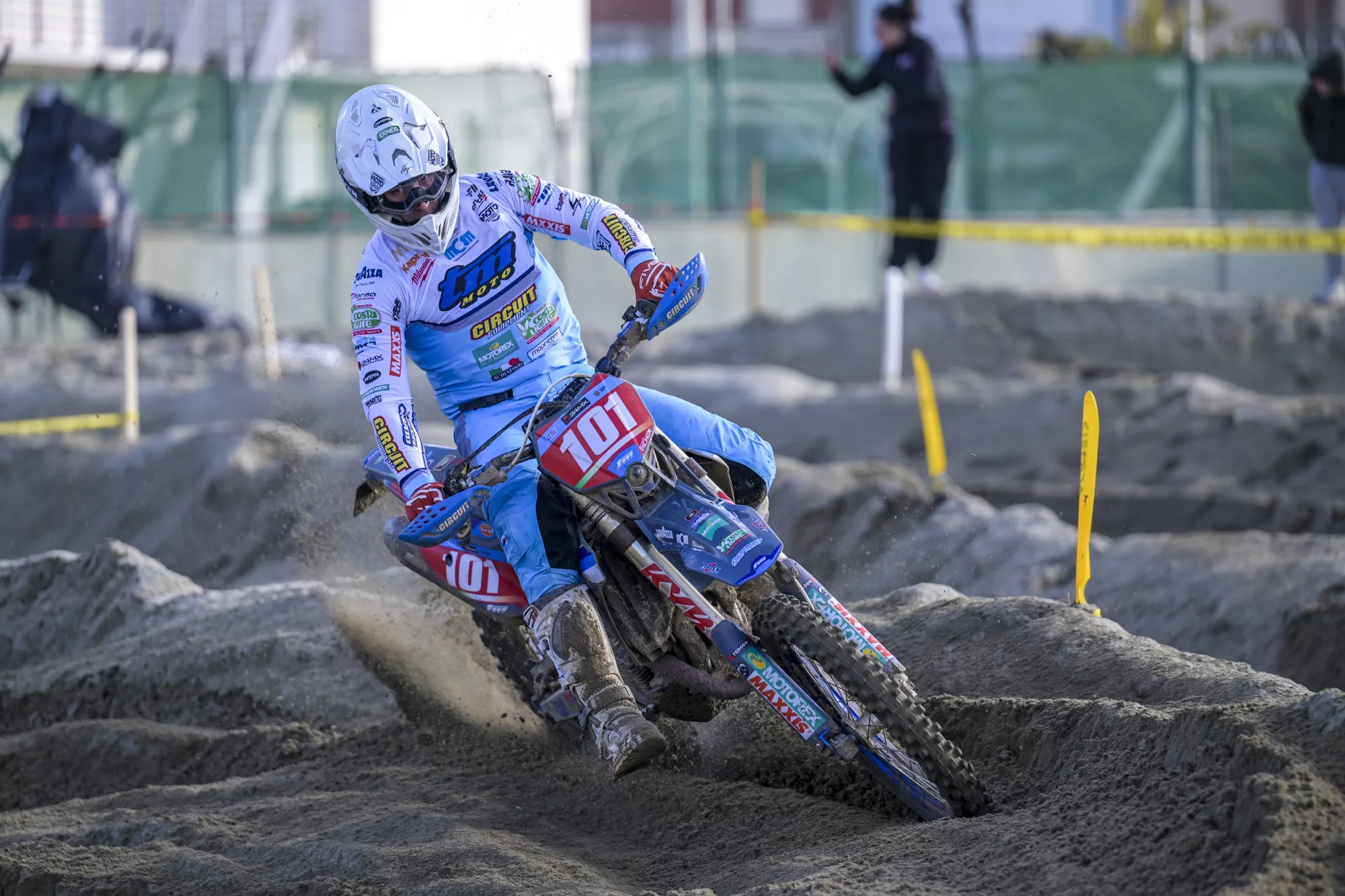 Motorcrosser met nummer 101 manoeuvreert krachtig door een bocht op een zanderig circuit tijdens een wedstrijd.