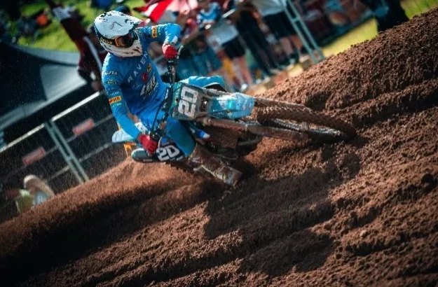 Motorcrosser met nummer 20 stuurt door een diepe bocht in een zanderig parcours tijdens een wedstrijd.
