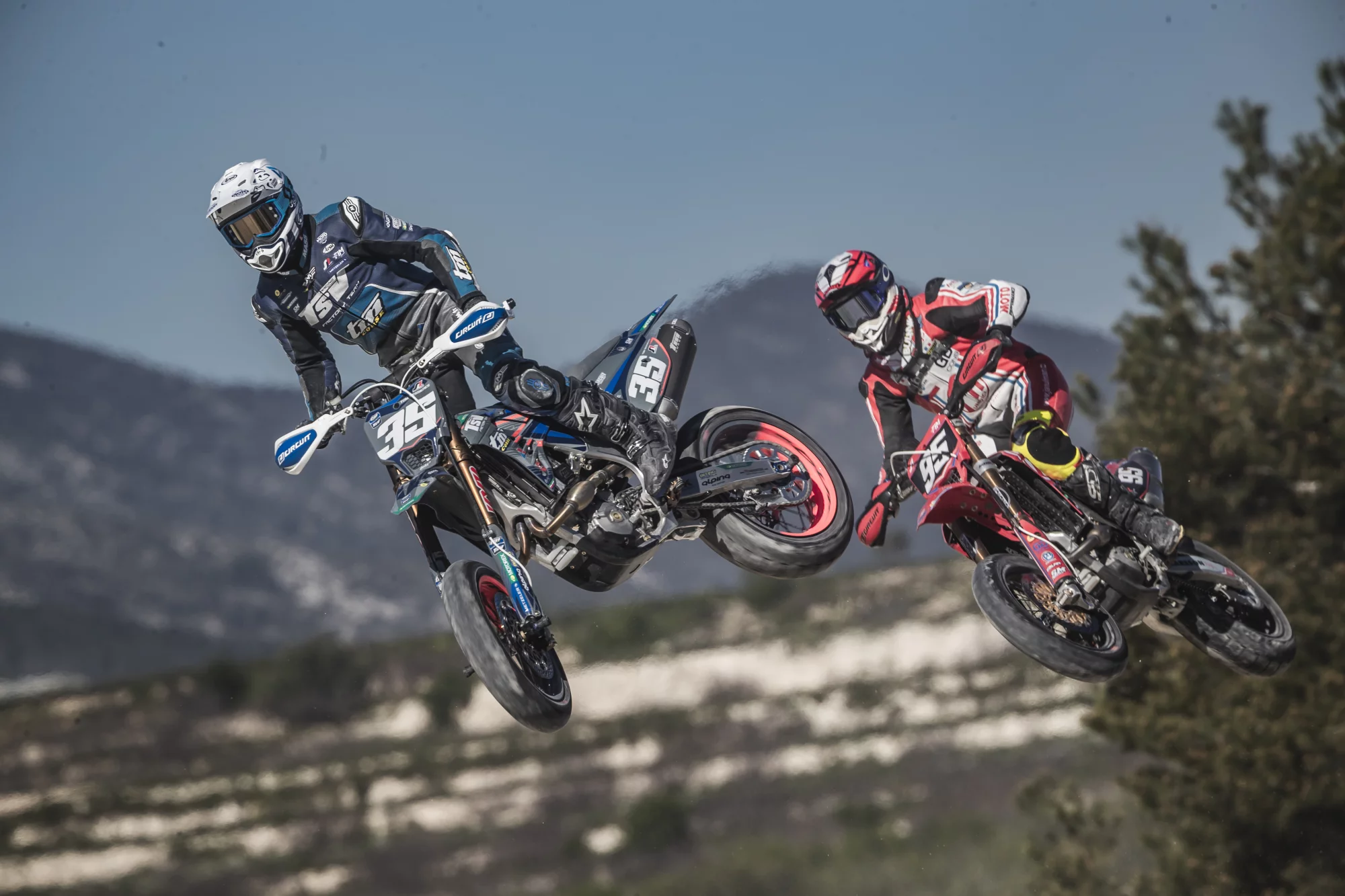 Twee supermoto-rijders met nummers 35 en 95 springen door de lucht tijdens een race.